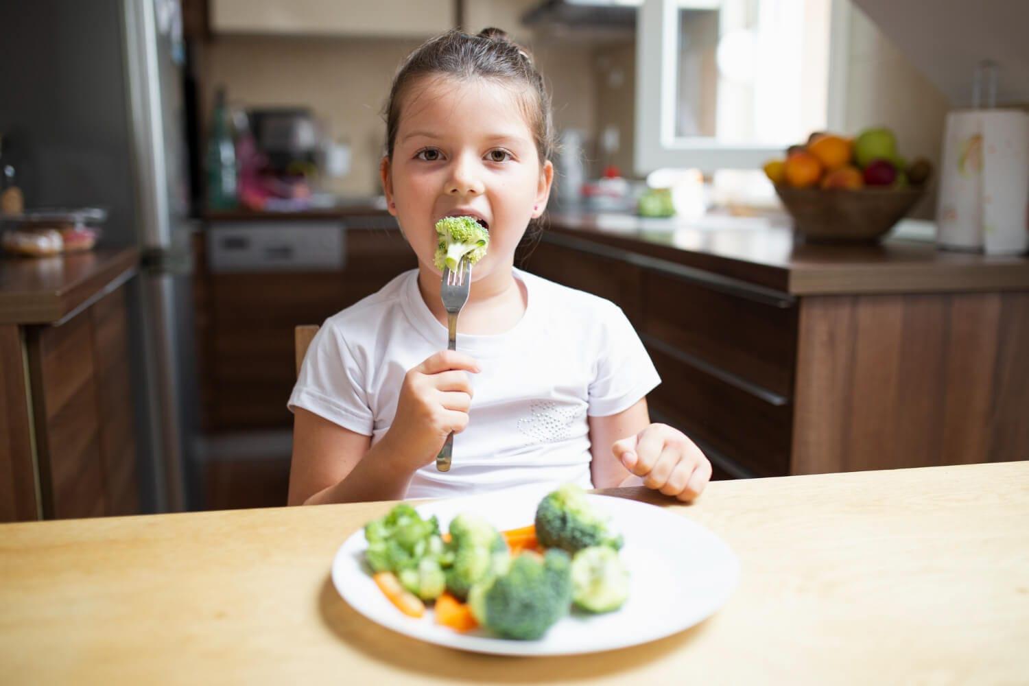 Little girl eating healthy vegetables at home - food that are good to fight with adhd