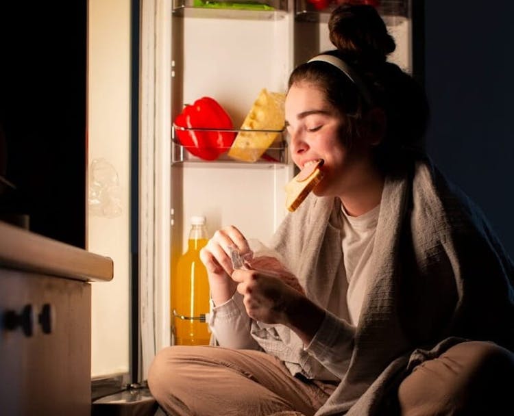 Women eating food from refrigerator at night who got a eating disorder with a blanked on her