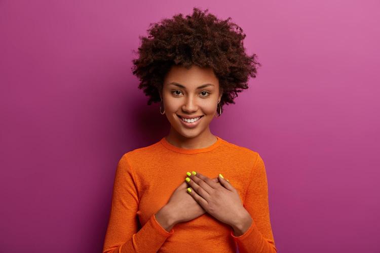 girl in orange jumper presses palms to heart, makes thankful gesture - practice gratitude to improve your mental health